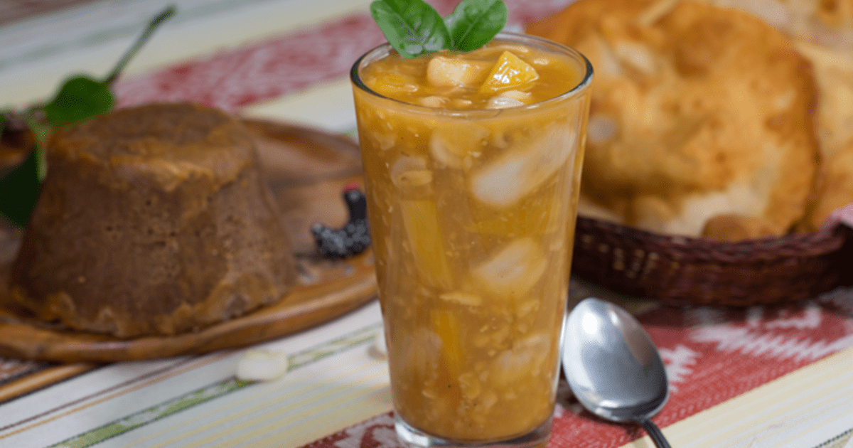 Champús is shown in a glass as a light yellow drink where you can see small pieces of fruit that look very refreshing.